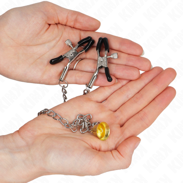 Zwei Nippelklemmen Kink Nipple Grip, verbunden durch eine Kette mit einem goldenen Glöckchen